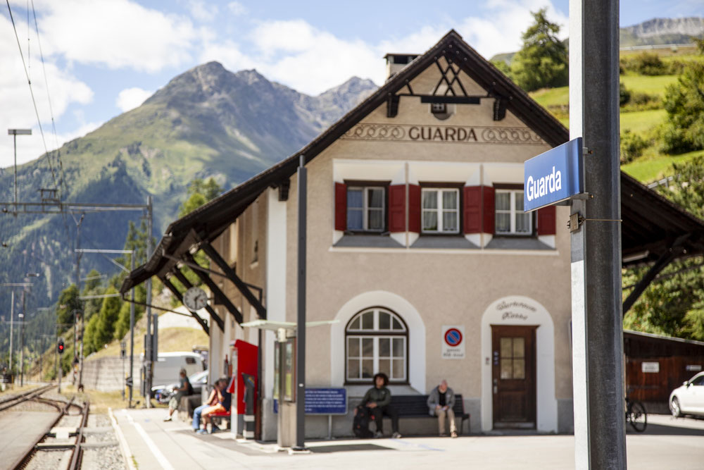 Bahngleise mit Bahnhofsgebäude, im Hintergrund Berge